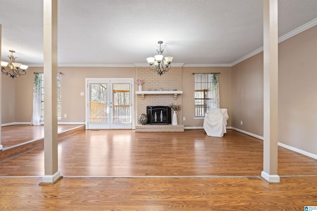 unfurnished living room with a chandelier, a brick fireplace, wood finished floors, and a healthy amount of sunlight