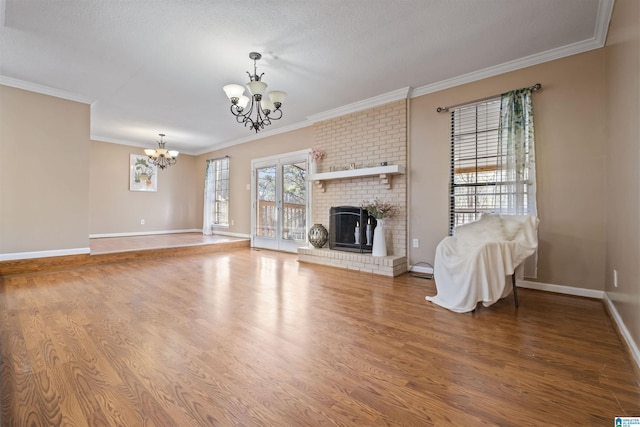 unfurnished living room featuring a chandelier, a fireplace, wood finished floors, baseboards, and ornamental molding