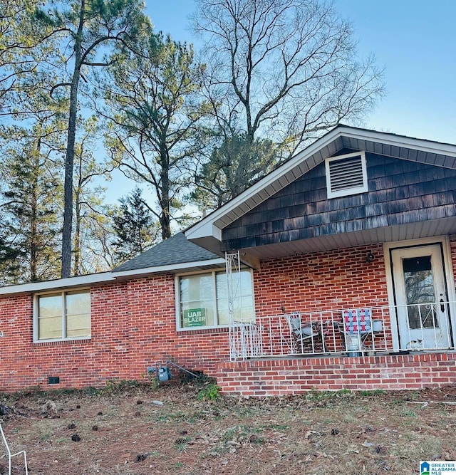 view of home's exterior with brick siding, crawl space, and a shingled roof