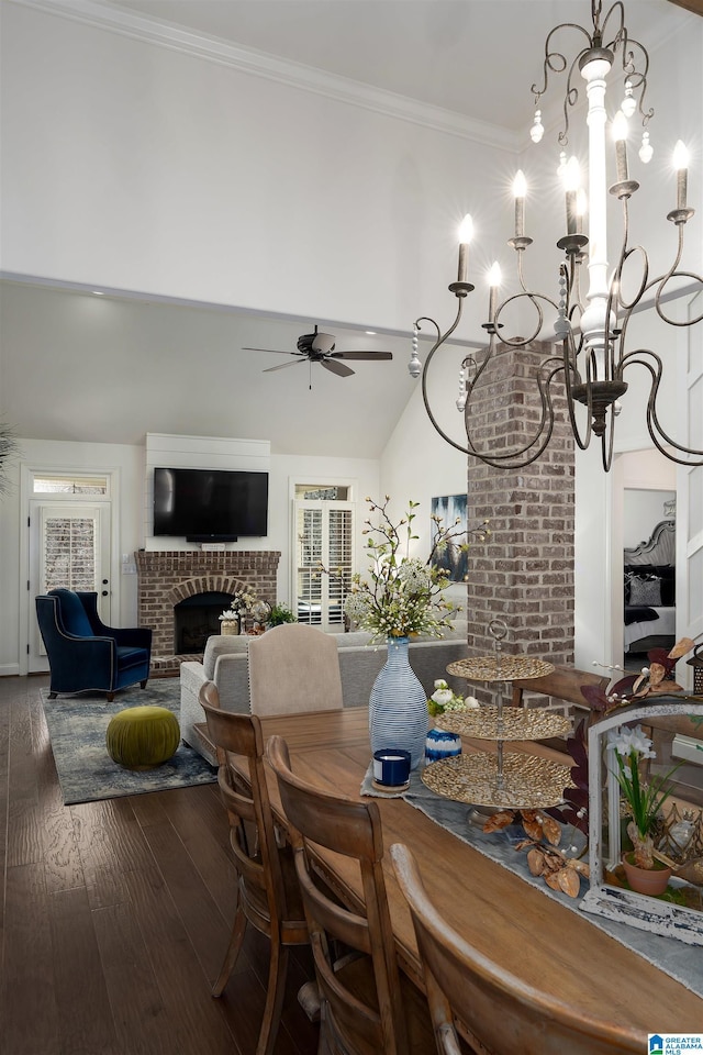 dining space with dark wood-type flooring, ornamental molding, a towering ceiling, a fireplace, and ceiling fan with notable chandelier