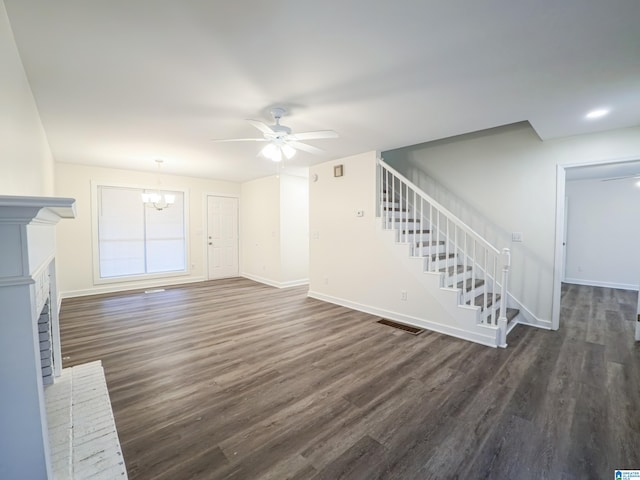 unfurnished living room with a brick fireplace, ceiling fan with notable chandelier, and dark hardwood / wood-style floors