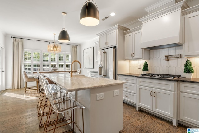 kitchen with custom exhaust hood, an island with sink, pendant lighting, stainless steel appliances, and white cabinets