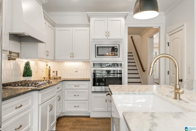 kitchen with sink, custom exhaust hood, ornamental molding, appliances with stainless steel finishes, and white cabinets