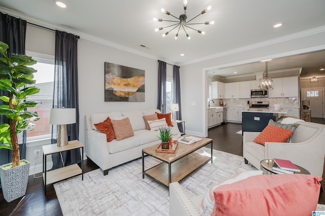 living room featuring a notable chandelier, hardwood / wood-style flooring, ornamental molding, and sink