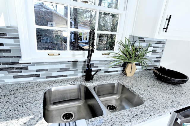 room details featuring tasteful backsplash, sink, white cabinets, and light stone counters