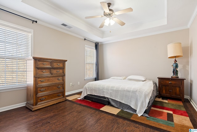 bedroom featuring dark wood-type flooring, ceiling fan, ornamental molding, and a tray ceiling