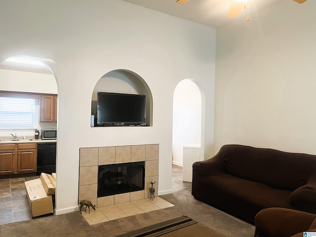 carpeted living room with a tile fireplace, sink, and ceiling fan