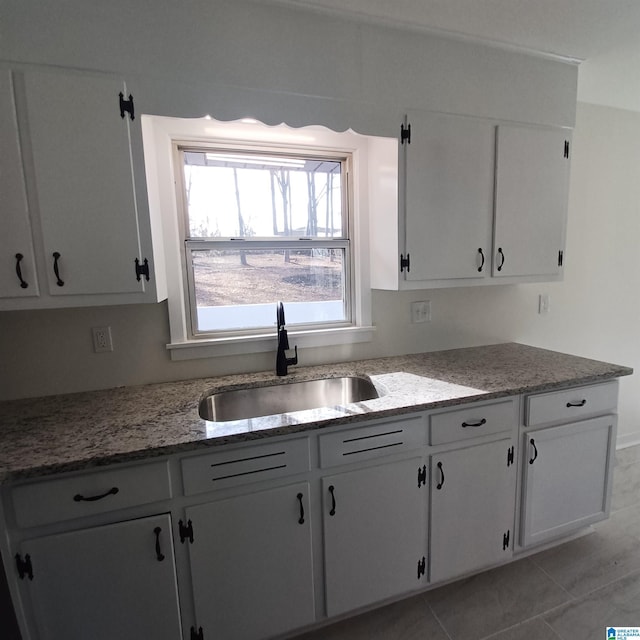 kitchen featuring white cabinetry, sink, light tile patterned floors, and dark stone counters