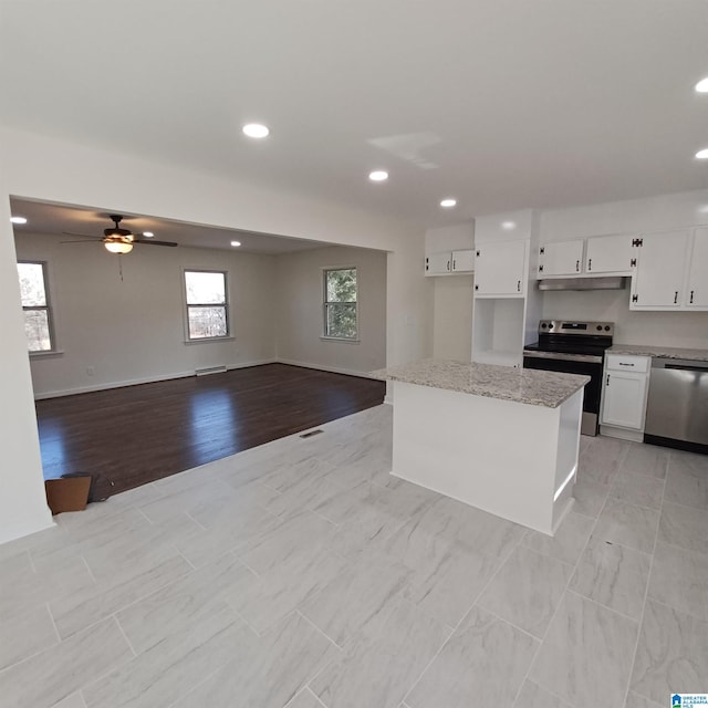 kitchen featuring ceiling fan, appliances with stainless steel finishes, white cabinetry, a center island, and light stone counters