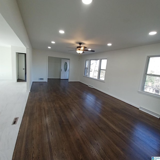 unfurnished living room featuring a baseboard heating unit, dark wood-type flooring, a wealth of natural light, and ceiling fan