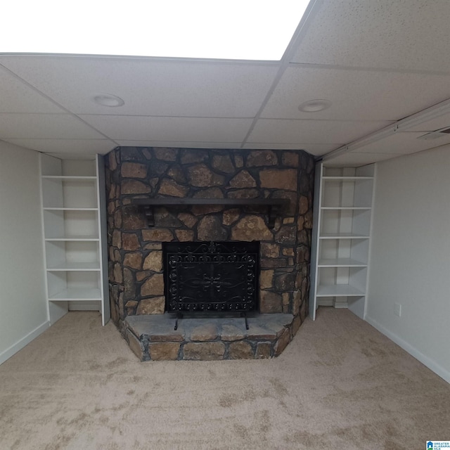 unfurnished living room with a stone fireplace, carpet flooring, and built in features