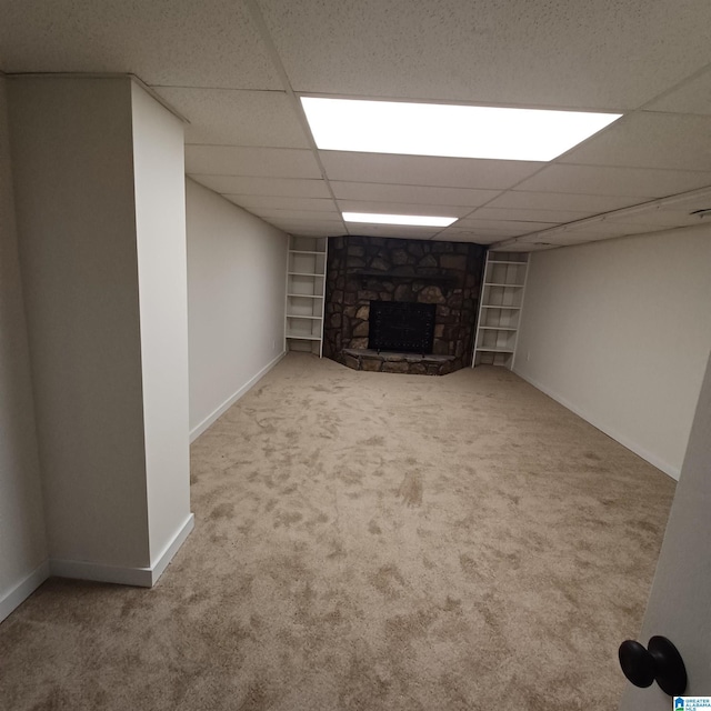 basement with carpet flooring, a stone fireplace, a paneled ceiling, and built in features