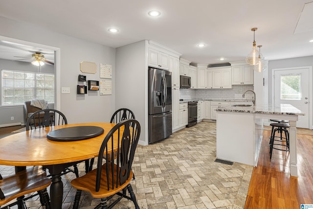 kitchen with decorative light fixtures, sink, white cabinets, light stone counters, and stainless steel appliances