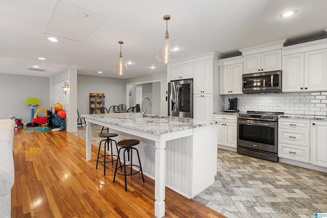 kitchen with backsplash, stainless steel appliances, light stone countertops, an island with sink, and white cabinets