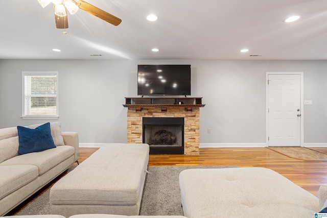 living room with ceiling fan, a stone fireplace, and hardwood / wood-style floors