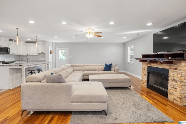 living room featuring ceiling fan, a stone fireplace, sink, and light hardwood / wood-style floors