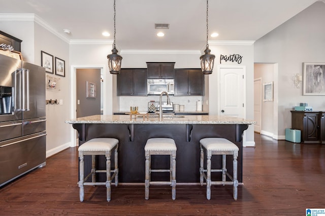 kitchen with stainless steel appliances, light stone countertops, hanging light fixtures, and a center island with sink