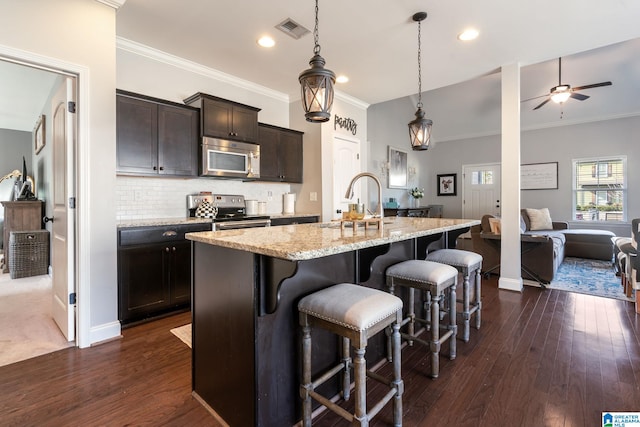 kitchen with sink, stainless steel appliances, a kitchen breakfast bar, an island with sink, and decorative light fixtures