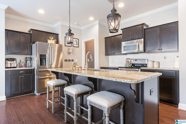 kitchen featuring a kitchen island with sink, sink, stainless steel appliances, and hanging light fixtures