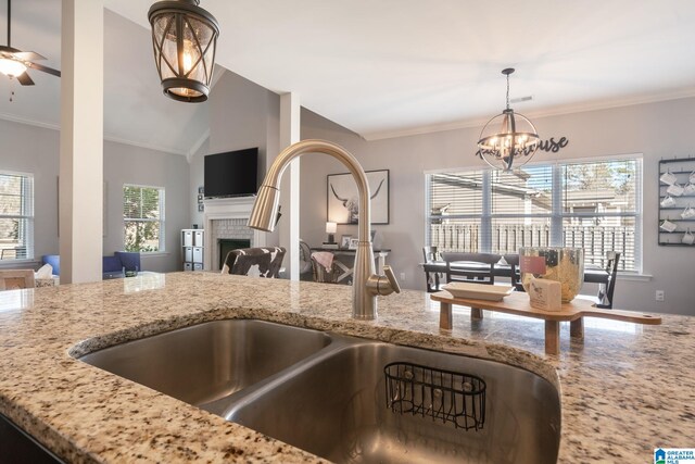 kitchen featuring a tiled fireplace, decorative light fixtures, light stone countertops, and sink