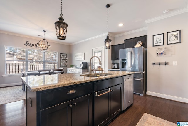 kitchen featuring appliances with stainless steel finishes, decorative light fixtures, sink, light stone countertops, and a center island with sink