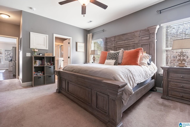 bedroom featuring ensuite bathroom, light colored carpet, and ceiling fan