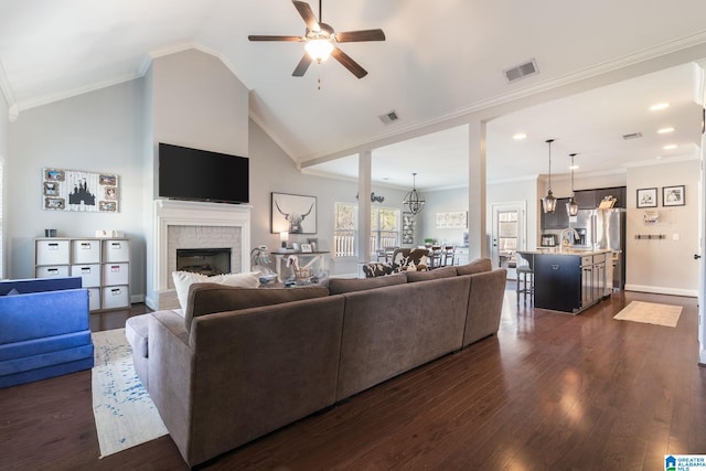 living room featuring high vaulted ceiling, dark hardwood / wood-style floors, a fireplace, ornamental molding, and ceiling fan with notable chandelier