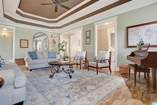 living room featuring crown molding, light hardwood / wood-style flooring, ceiling fan, and a tray ceiling