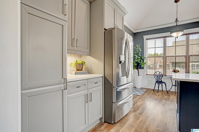 kitchen featuring crown molding, vaulted ceiling, stainless steel fridge with ice dispenser, pendant lighting, and light hardwood / wood-style floors