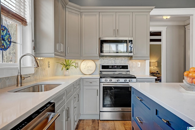 kitchen with blue cabinets, sink, light hardwood / wood-style flooring, stainless steel appliances, and decorative backsplash