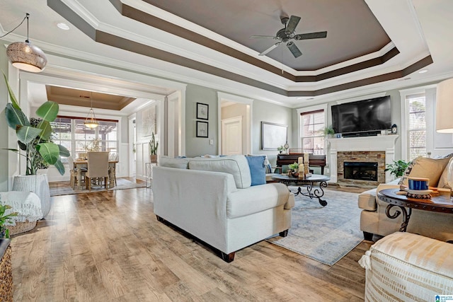 living room with a tray ceiling, a fireplace, ceiling fan, and light wood-type flooring