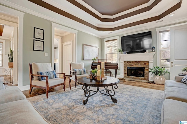 living room with a fireplace, a tray ceiling, wood-type flooring, and ornamental molding