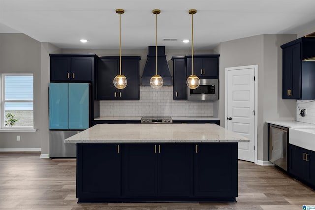 kitchen with hanging light fixtures, appliances with stainless steel finishes, a center island, and custom range hood