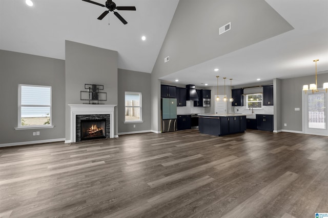 unfurnished living room featuring a fireplace, high vaulted ceiling, dark hardwood / wood-style floors, and ceiling fan with notable chandelier