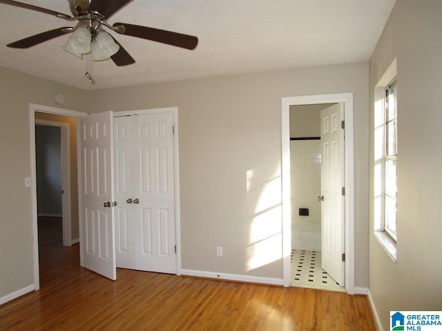 unfurnished bedroom with multiple windows, wood-type flooring, connected bathroom, and a closet