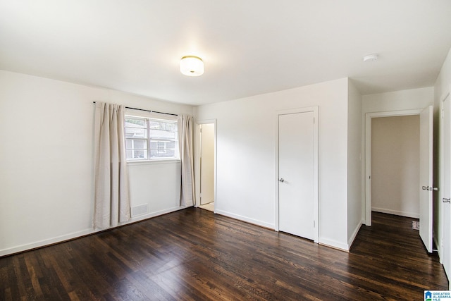 unfurnished bedroom with dark wood-style floors, visible vents, and baseboards