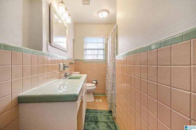 full bath featuring toilet, a wainscoted wall, visible vents, vanity, and tile walls