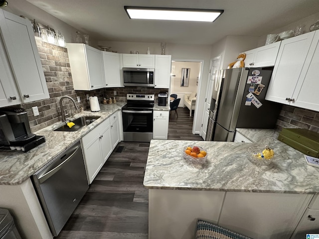 kitchen with appliances with stainless steel finishes, tasteful backsplash, white cabinetry, sink, and light stone countertops