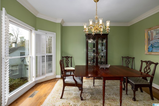 dining room with a notable chandelier, crown molding, and light hardwood / wood-style flooring