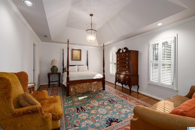 bedroom with hardwood / wood-style floors, a notable chandelier, ornamental molding, and a raised ceiling