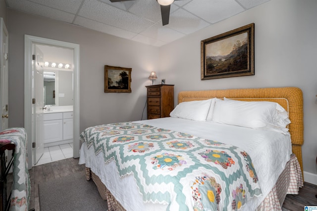 bedroom featuring wood-type flooring, ensuite bathroom, a drop ceiling, and ceiling fan