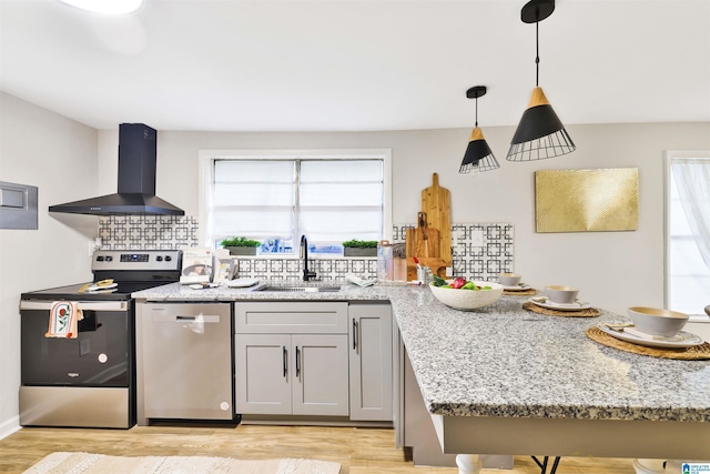 kitchen with pendant lighting, stainless steel appliances, light stone counters, and wall chimney range hood