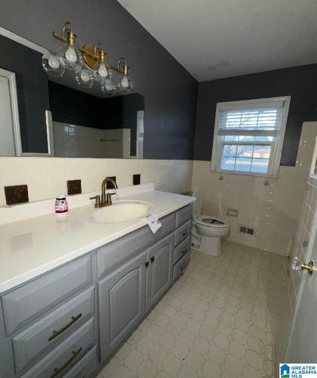 bathroom featuring visible vents, toilet, a wainscoted wall, vanity, and tile walls