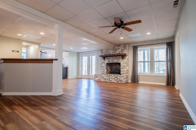 unfurnished living room with ceiling fan, a large fireplace, a wealth of natural light, and dark wood-type flooring