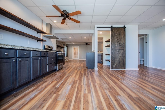 unfurnished living room with a drop ceiling, dark wood-type flooring, a barn door, and ceiling fan