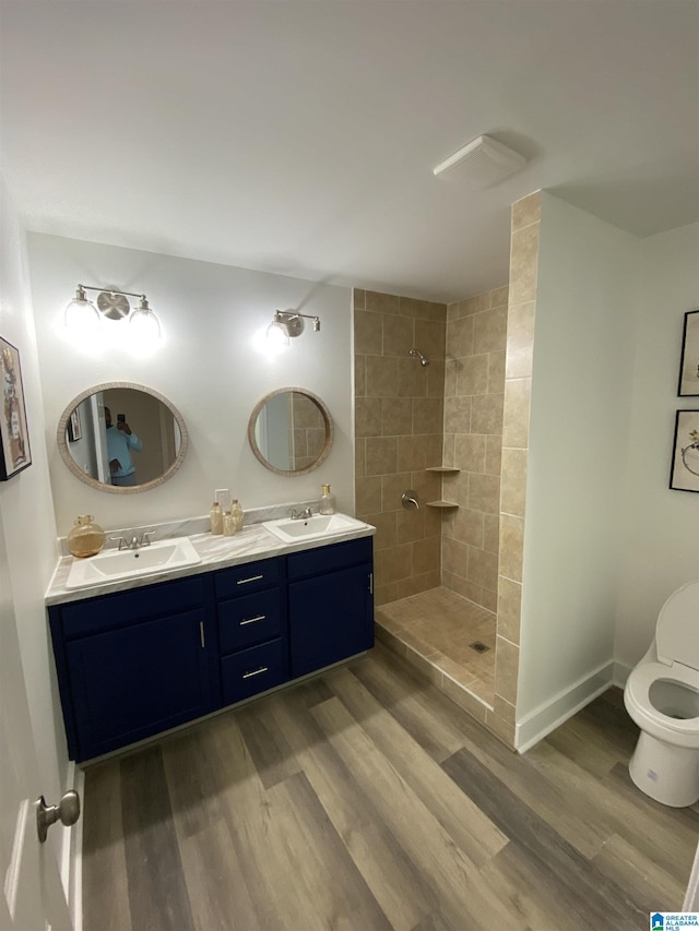 bathroom featuring hardwood / wood-style floors, toilet, a tile shower, and vanity