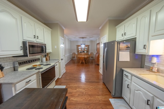 kitchen with white cabinetry, hardwood / wood-style floors, stainless steel appliances, ornamental molding, and decorative light fixtures