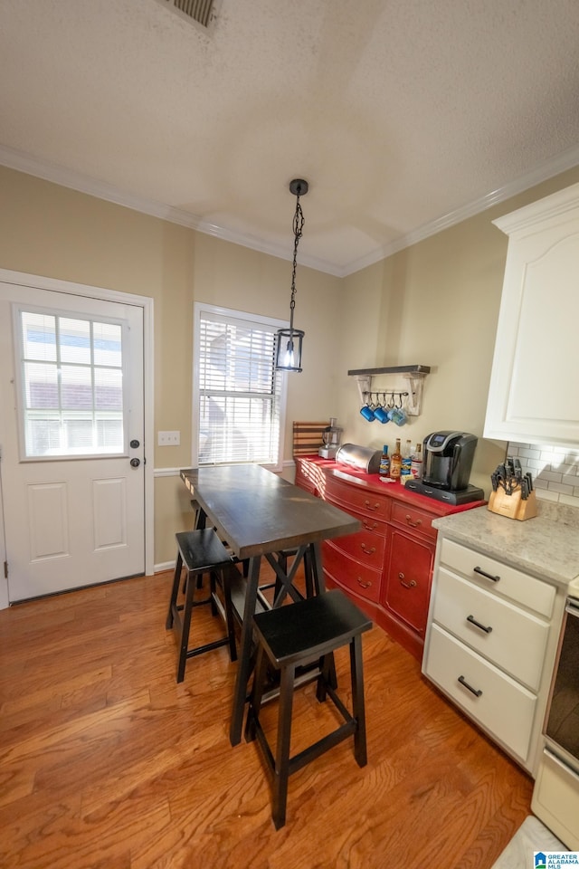 dining area with ornamental molding, light hardwood / wood-style floors, and a textured ceiling