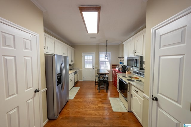 kitchen featuring crown molding, hardwood / wood-style flooring, appliances with stainless steel finishes, pendant lighting, and white cabinets