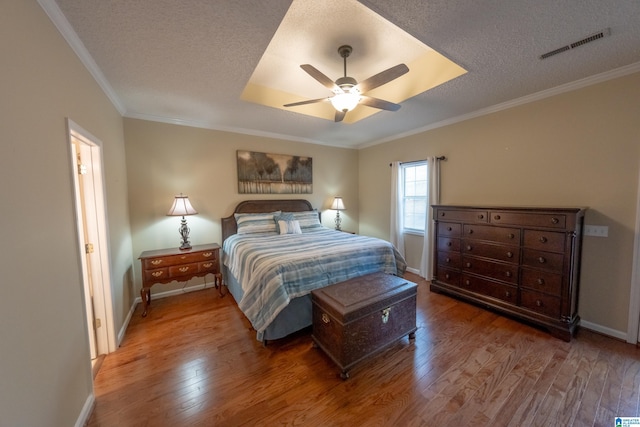 bedroom featuring hardwood / wood-style flooring, ornamental molding, ceiling fan, a raised ceiling, and a textured ceiling